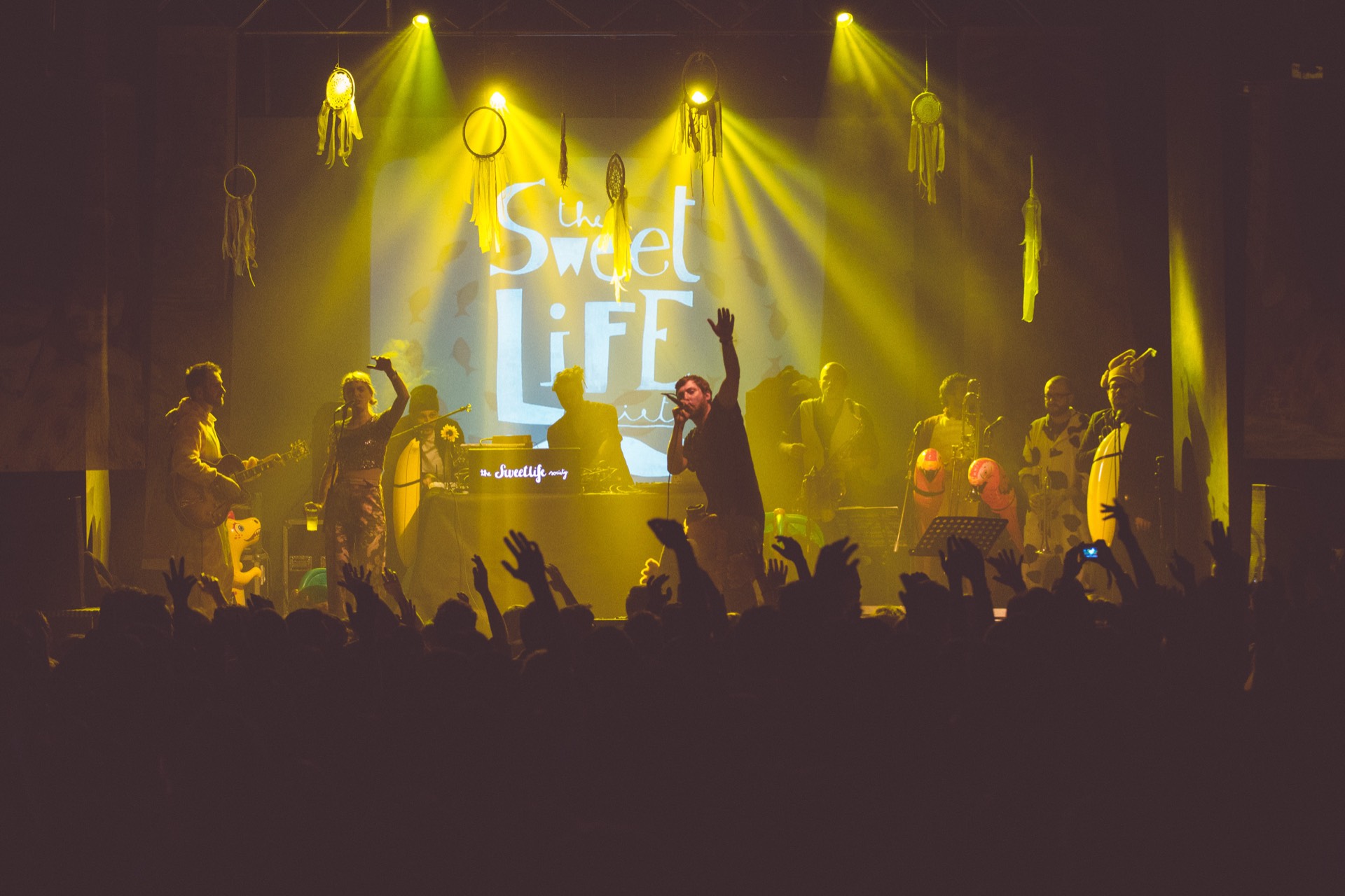 The band on stage under the Sweet Life backdrop in golden light